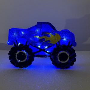 Pu&ograve; includere: Luce notturna a forma di monster truck blu con fiamme dorate e luci LED.