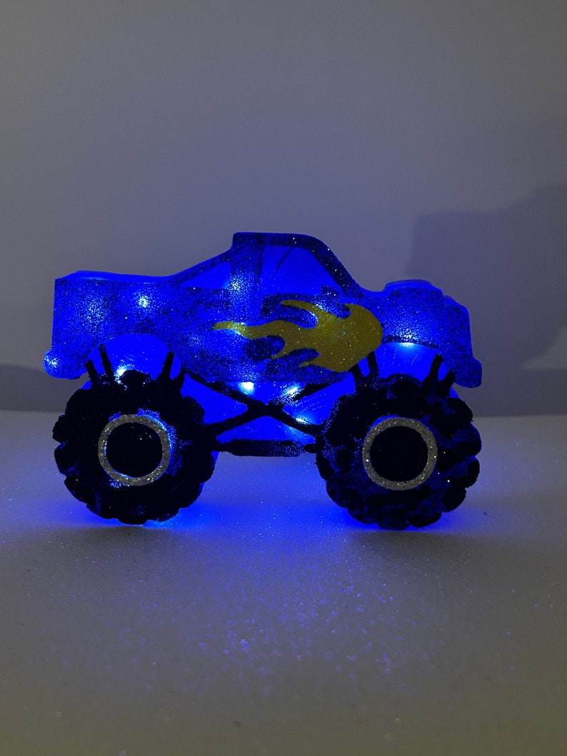Pu&ograve; includere: Luce notturna a forma di monster truck blu con fiamme dorate e luci LED.