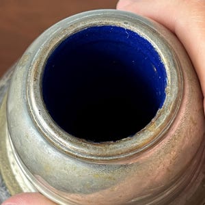 May include: Close-up of a silver-colored container with a dark blue interior. The container has a wide, circular opening and a slightly textured surface. The interior is a deep, rich blue color.