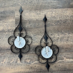 May include: A pair of black metal wall sconces with a decorative scroll design and silver candle holders.