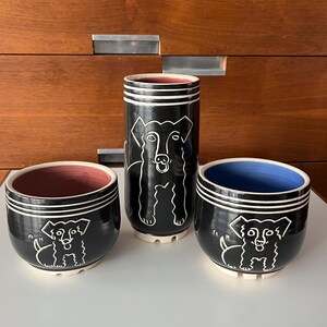 May include: Three black ceramic planters with white dog illustrations. The planters are different sizes and have a glossy finish. The largest planter has a dog with its head tilted up, while the two smaller planters have dogs with their heads facing forward.