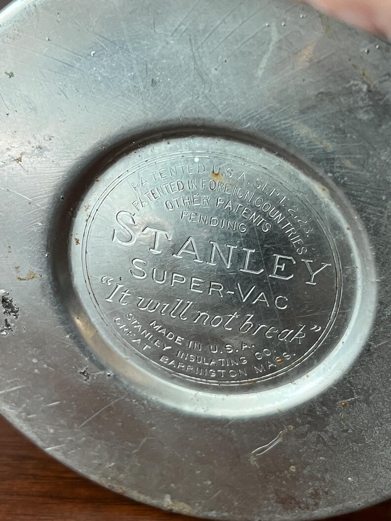 May include: Close-up of a vintage Stanley Super-Vac thermos base. The silver-colored metal base features embossed text including "Stanley Super-Vac" and "It will not break." Made in U.S.A.