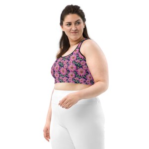 May include: A woman wearing a navy blue and pink floral print sports bra with a white tank top underneath. She is wearing white pants.