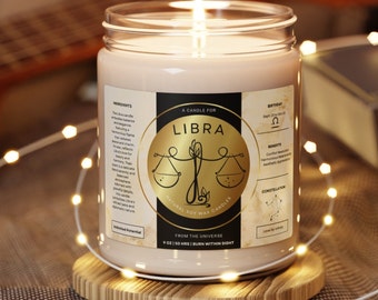 Könnte beinhalten: Ein braunes Glas-Kerzengefäß mit einem weißen Deckel und einem goldenen Etikett mit der Aufschrift "A Candle For Libra" und einem Waage-Sternzeichen. Die Kerze ist angezündet und die Flamme ist sichtbar. Das Etikett enthält auch die Geburtsdaten, Vorteile, die Konstellation und "Natural Soy Wax Candles".