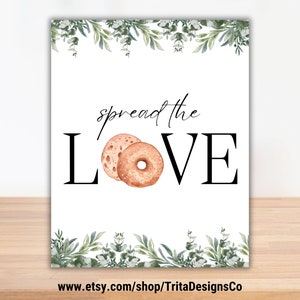 May include: A white printable sign with a green leafy border. The sign says "spread the LOVE" with two brown and orange bagels in the middle of the word LOVE. The text at the bottom of the sign says "www.etsy.com/shop/TritaDesignsCo"