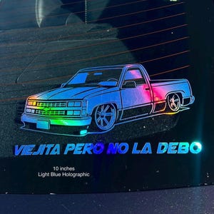 May include: Light blue holographic truck sticker, measuring 25.4 cm, with the text "Viejita Pero No La Debo". The sticker depicts a detailed illustration of a classic pickup truck.