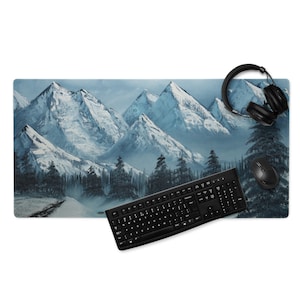Puede incluir: Una alfombrilla de escritorio rectangular con una pintura de paisaje de montaña en tonos azules y blancos. Un teclado, un ratón y unos auriculares negros están sobre la alfombrilla. La alfombrilla proporciona una superficie lisa para el uso del ordenador.