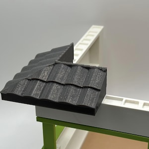 May include: A black plastic roof corner piece for a model house. The roof has a textured, shingled design.