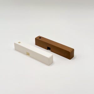 Könnte beinhalten: Zwei rechteckige Holzobjekte, eines weiß und eines braun, werden auf einer weißen Oberfläche gezeigt. Jedes hat einen Ausschnitt und ein kleines quadratisches Loch. Das braune Objekt ist dunkler als das weiße.