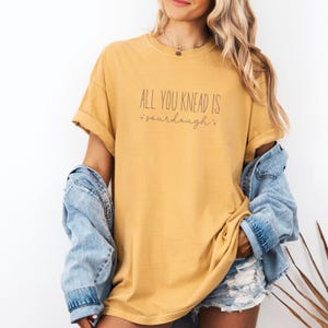 May include: A mustard yellow t-shirt with the text "All you knead is *sourdough*" printed on the front.