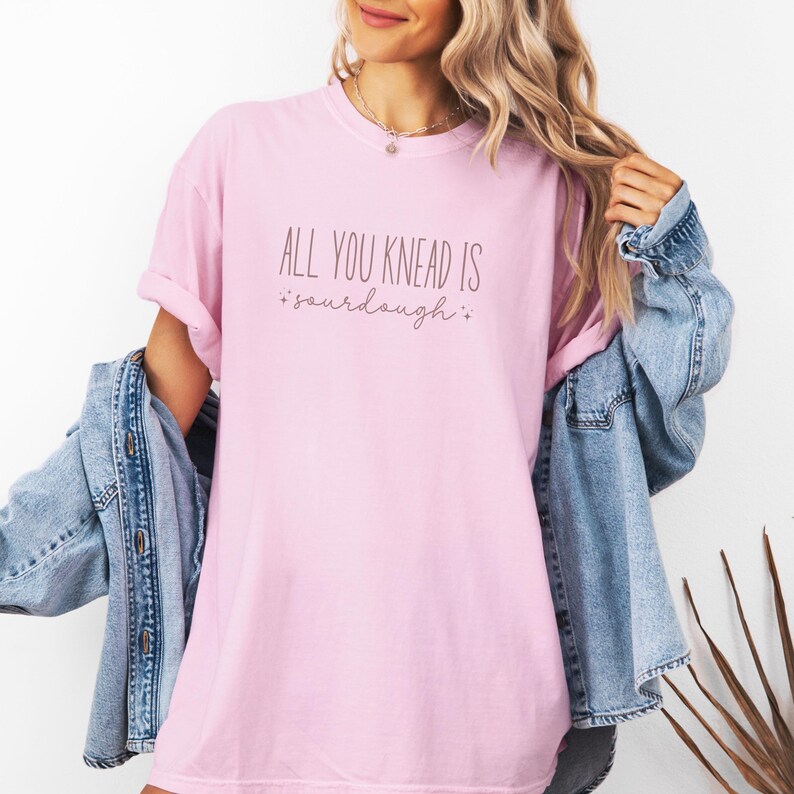 May include: A pink t-shirt with the text "All you knead is sourdough" in a light brown color.