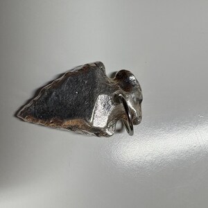 May include: A silver arrowhead pendant with a loop for a chain. The arrowhead is a rough, irregular shape.