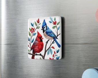 May include: A blue jay and a cardinal perched on a branch with red and white flowers. The birds are surrounded by green leaves.