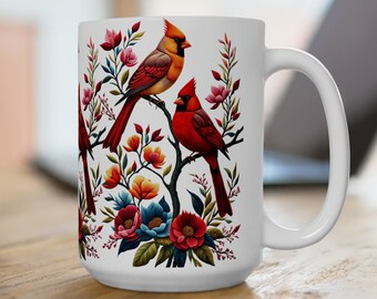 May include: White ceramic mug with a colorful floral design featuring red cardinals perched on branches. The flowers are in shades of pink, red, blue, and yellow.