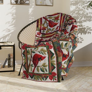 May include: A red and green quilted throw blanket with a pattern of cardinals and leaves. The blanket is draped over a chair.