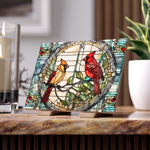 Op de afbeelding: Een glas-in-loodpaneel met twee kardinaals, een rode en een gele, die op een tak met groene bladeren zitten. Het paneel is omlijst met een decoratieve rand met blauwe en groene accenten.