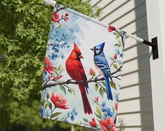 May include: A watercolor garden flag featuring a blue jay and a cardinal perched on a branch with pink and blue flowers. The background is a light blue watercolor wash.