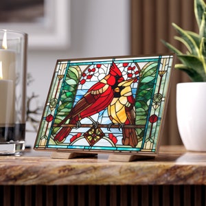 Può includere: Un pannello di vetro colorato che raffigura due cardinali rossi appollaiati su un ramo con foglie verdi e bacche rosse. Il pannello è incorniciato da una cornice in legno marrone e ha un supporto decorativo.