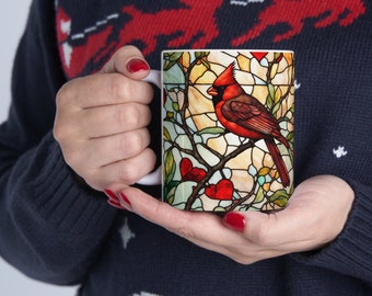 May include: White ceramic mug with a stained glass design featuring a red cardinal bird perched on a branch with red hearts. The background is a blue and green stained glass pattern.