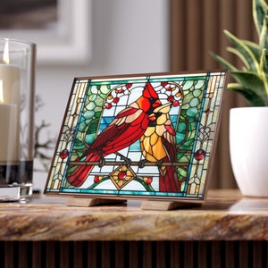 Puede incluir: Un panel de vitral que representa dos cardenales rojos posados en una rama con hojas verdes y bayas rojas. Los cardenales están rodeados por un borde decorativo.