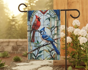 May include: A stained glass style garden flag featuring a cardinal and a blue jay perched on a branch. The flag has a blue, green, and red color scheme.