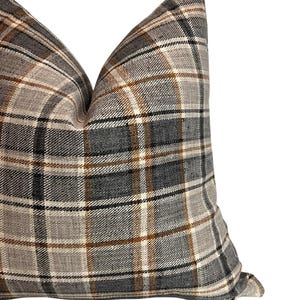 May include: A gray, brown, and white plaid pillow with a square shape. The pillow is made of a soft, textured fabric.