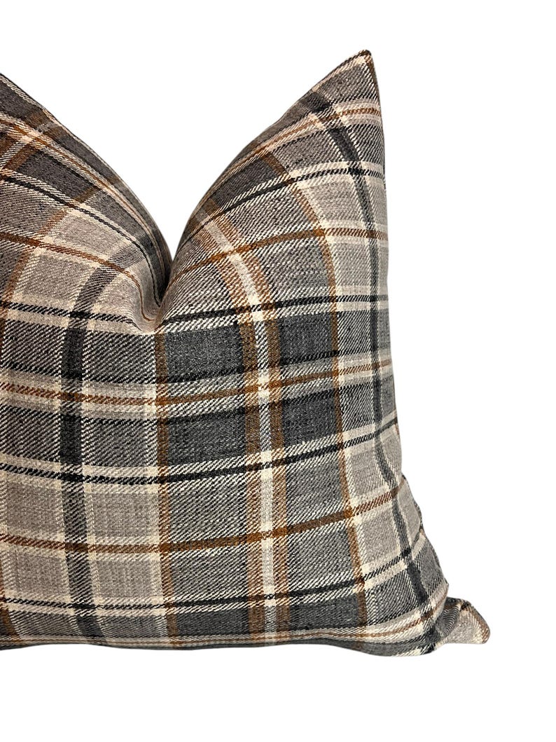 May include: A gray, brown, and white plaid pillow with a square shape. The pillow is made of a soft, textured fabric.