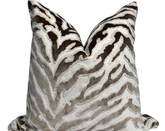 Könnte beinhalten: Ein quadratisches Zierkissen mit Zebra-Streifenmuster in Braun-, Beige- und Weißtönen. Das Kissen hat eine strukturierte Oberfläche und dient dekorativen Zwecken. Es strahlt Komfort und Stil aus.