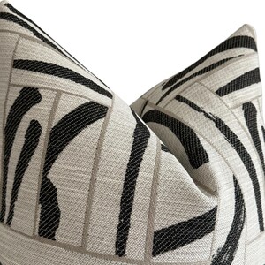 May include: Close-up of two decorative throw pillows. The pillows feature a cream-colored background with a bold black and gray geometric pattern. The design includes thick black stripes and gray rectangular lines.