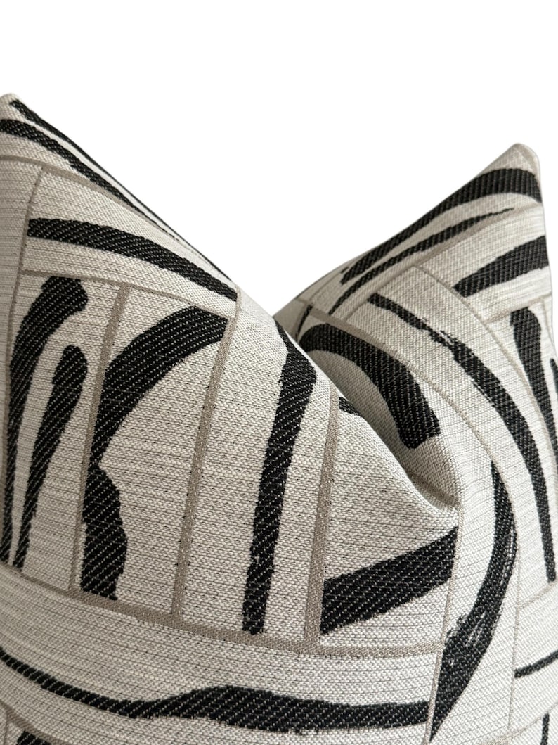 May include: Close-up of two decorative throw pillows. The pillows feature a cream-colored background with a bold black and gray geometric pattern. The design includes thick black stripes and gray rectangular lines.