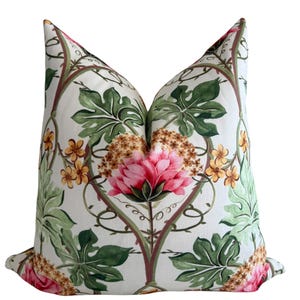 May include: A square throw pillow featuring a white background with a repeating botanical pattern. The design includes large pink peony-like flowers, clusters of small yellow blossoms, and green lobed leaves connected by thin, dark brown vines.