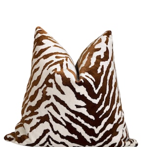 May include: A square throw cushion featuring a brown and white zebra stripe pattern. The fabric has a soft, velvet-like texture with a distinct pile. The cushion is plumped in the centre, creating a slight indentation at the top edge.