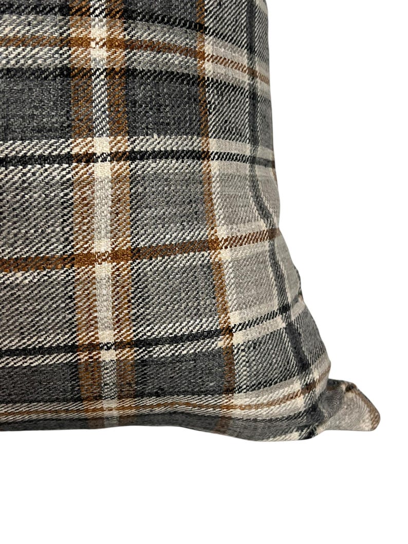 May include: Close-up of a gray, brown, and white plaid pillow cover. The fabric has a woven texture.