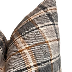 May include: Close-up of a gray, brown, and white plaid pillow cover. The fabric has a woven texture.