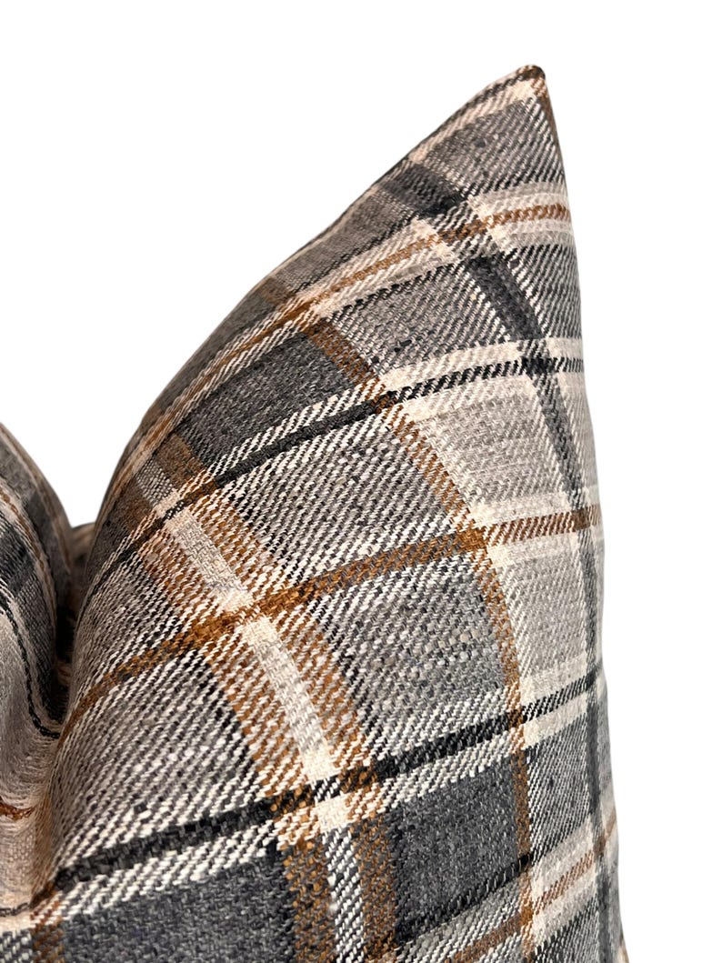 May include: Close-up of a gray, brown, and white plaid pillow cover. The fabric has a woven texture.