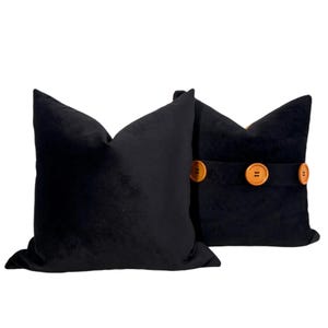 Puede incluir: Dos almohadas de terciopelo negro con detalles de botones marrones. Las almohadas son cuadradas y tienen una textura suave y mullida.
