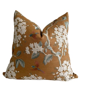 Pode incluir: Almofada decorativa quadrada com fundo mostarda. Apresenta um bordado de flores brancas, folhas verde-azuladas e pássaros em tons de vermelho, azul e castanho. Ideal para sofá ou cama.