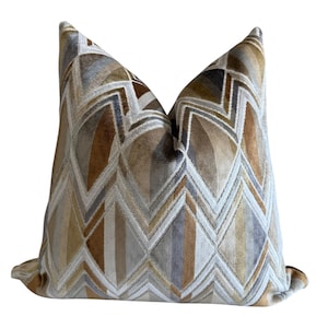 May include: A square throw pillow featuring a velvet-like texture with a repeating geometric chevron pattern in shades of tan, brown, cream, and grey. The design consists of interlocking zig-zag lines and diamond shapes across the entire surface.