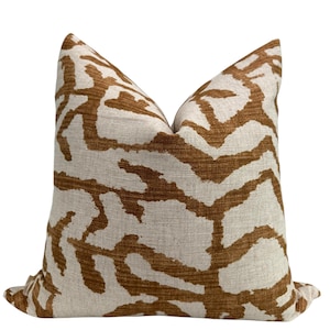 Puede incluir: Una almohada decorativa con fondo blanco y un patrón abstracto marrón. La almohada está hecha de una tela suave y texturizada.