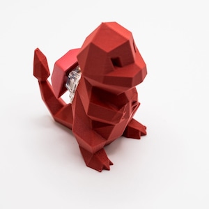 Op de afbeelding: Een rood, low-poly 3D-geprint beeldje van een Pokemon-personage. Het beeldje staat op een wit oppervlak.