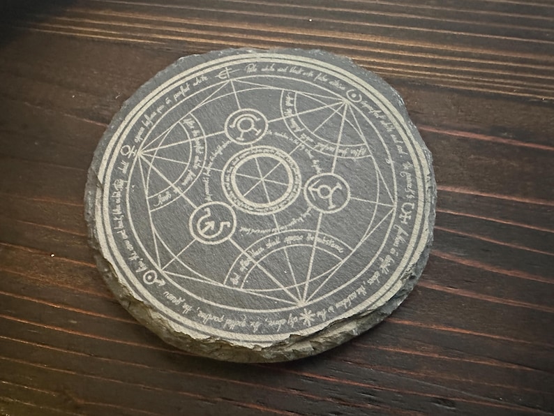 May include: A round, gray slate coaster with a white, engraved alchemical symbol. The symbol is surrounded by a circle of text in white.