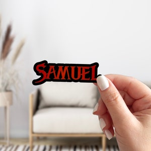 May include: A black and red vinyl sticker with the word "SAMUEL" in a bold, stylized font.