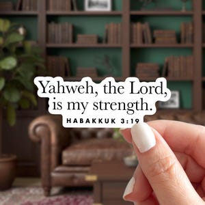 May include: A white sticker with the text "Yahweh, the Lord, is my strength." and the reference "HABAKKUK 3:19" in black. The sticker is held by a person with a blurred background of a room with bookshelves and a leather chair.
