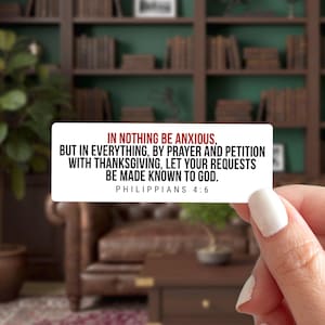May include: A rectangular white sticker with the text "IN NOTHING BE ANXIOUS, BUT IN EVERYTHING, BY PRAYER AND PETITION WITH THANKSGIVING, LET YOUR REQUESTS BE MADE KNOWN TO GOD. PHILIPPIANS 4:6" in black and red font. The sticker is held by a person.