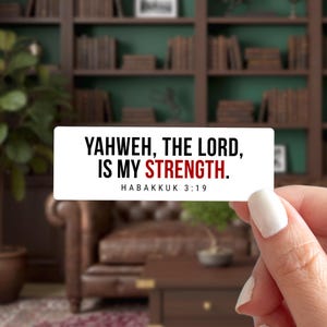 May include: A white rectangular sticker with the text "YAHWEH, THE LORD, IS MY STRENGTH." in black and red. The text "HABAKKUK 3:19" is below the main text. The sticker is held by a person.