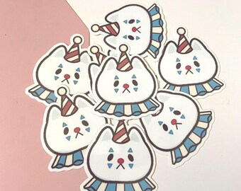May include: A collection of white cat stickers with clown-like features. Each sticker has a red nose, blue and red accents, and a striped party hat. The cats wear blue and white striped collars.