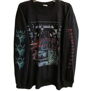 Puede incluir: Camiseta negra de manga larga con un estampado gráfico de un logotipo de banda y un patrón repetido de criaturas estilizadas en las mangas. El texto "R.A.R.E.R.A.R.E." está impreso en la camiseta.