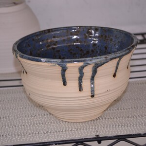 May include: A white ceramic bowl with a blue and brown glaze. The glaze has a speckled appearance and drips down the sides of the bowl.