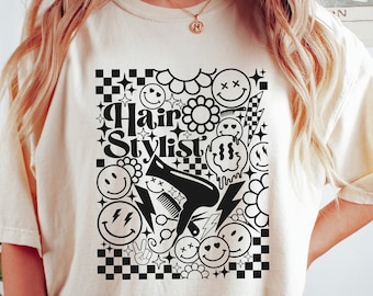 Könnte beinhalten: Ein weißes T-Shirt mit einem schwarzen Grafikdesign, das den Text "Hair Stylist" zeigt, umgeben von Smileys, Blumen, Blitzen und einem Haartrockner.