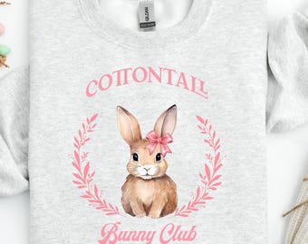Könnte beinhalten: Grauer Pullover mit einem rosa Kaninchen, das eine rosa Schleife in einem Kranz mit dem Text "Cottontail Bunny Club" trägt.